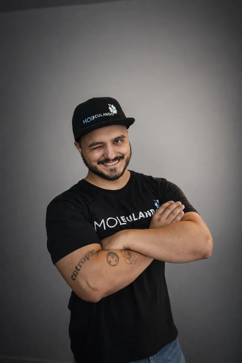 Prof. Lucas Moreno piscando e sorrindo, de braços cruzados